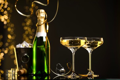 Photo of Champagne in glasses and ice bucket with bottle on mirror surface against black background with blurred lights