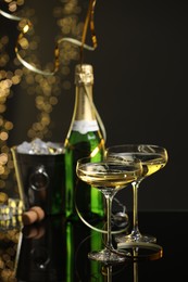 Photo of Champagne in glasses and ice bucket with bottle on mirror surface against black background with blurred lights