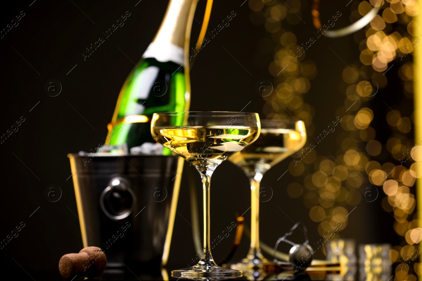 Photo of Champagne in glasses and ice bucket with bottle on dark background with blurred lights, closeup