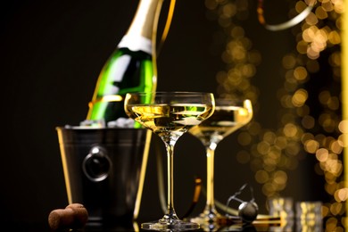 Photo of Champagne in glasses and ice bucket with bottle on dark background with blurred lights, closeup