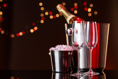 Photo of Glasses, bottle of Champagne and ice buckets on mirror surface against color background with blurred lights, space for text