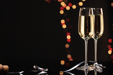 Photo of Champagne in glasses on mirror surface against black background with blurred lights, space for text