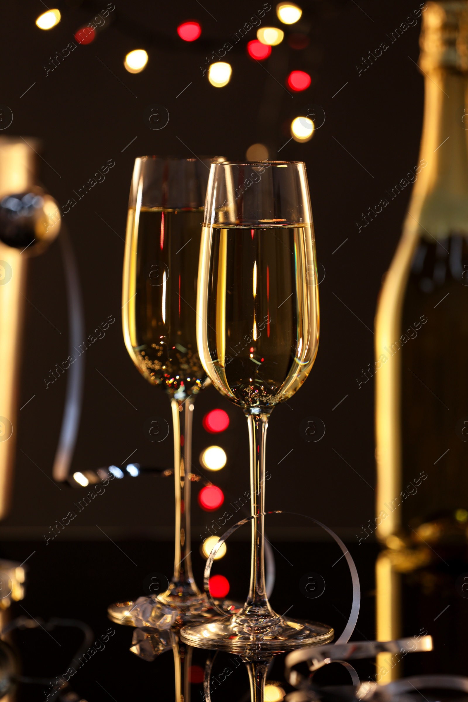 Photo of Champagne in glasses and bottle on black mirror surface