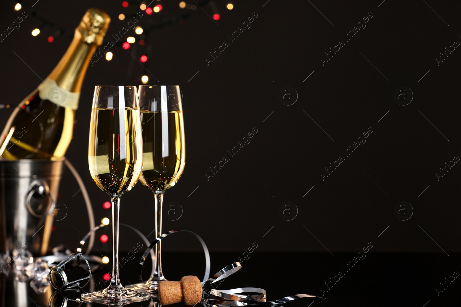 Photo of Champagne in glasses and ice bucket with bottle on black mirror surface, space for text