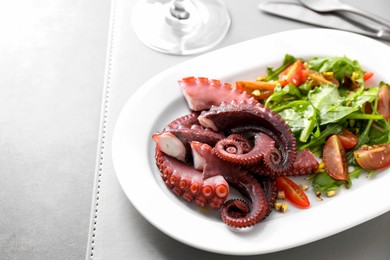 Photo of Plate with tasty boiled octopus tentacles and salad on grey table, closeup