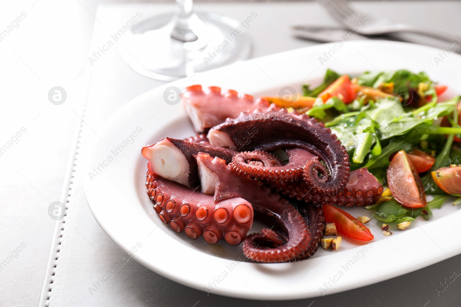 Photo of Plate with tasty boiled octopus tentacles and salad on grey table, closeup