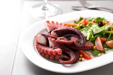 Photo of Plate with tasty boiled octopus tentacles and salad on grey table, closeup