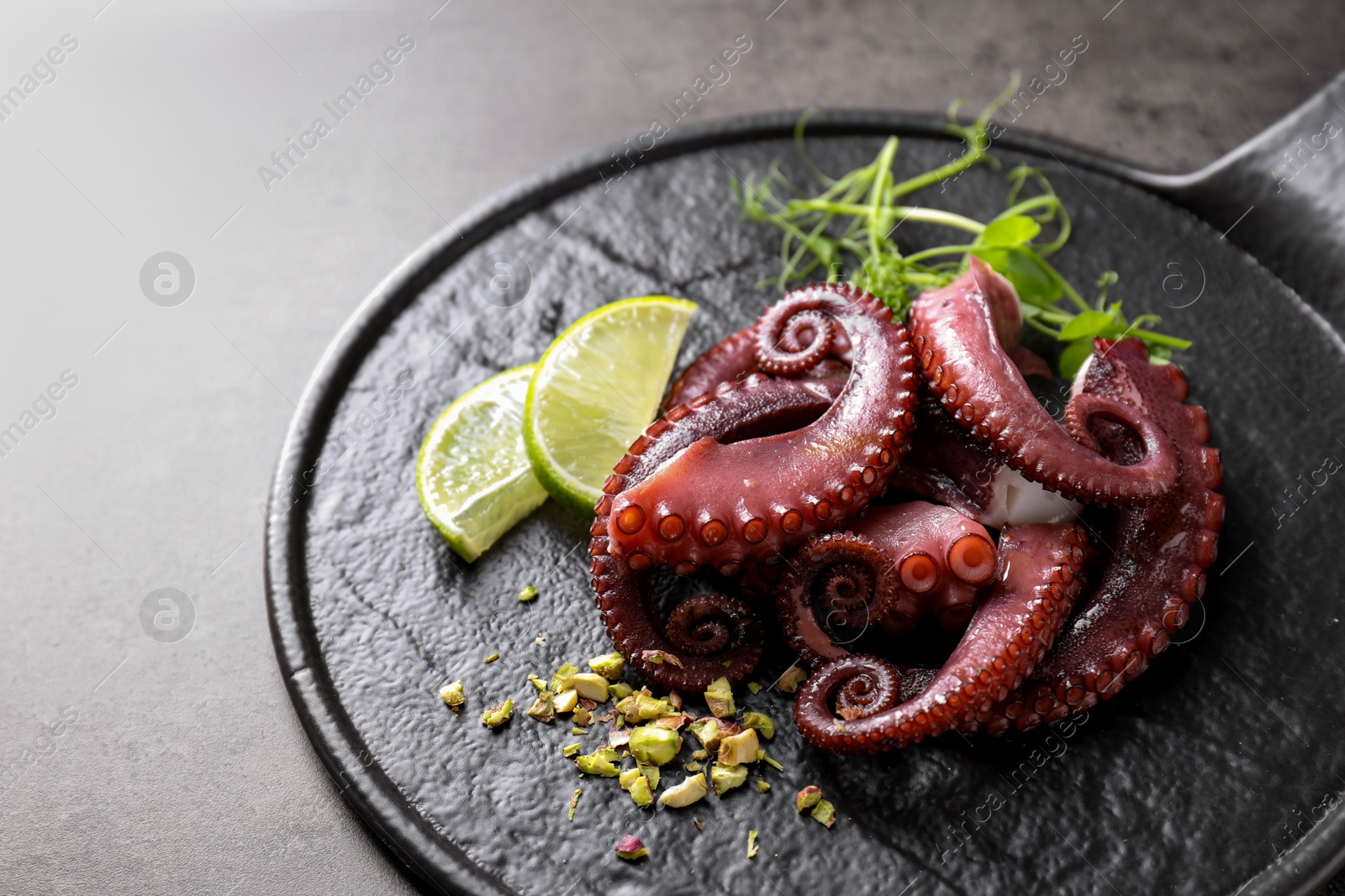 Photo of Tasty boiled octopus tentacles, microgreens, nuts and lime on grey table, closeup