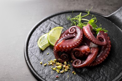 Photo of Tasty boiled octopus tentacles, microgreens, nuts and lime on grey table, closeup