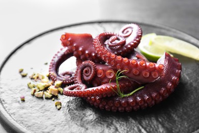 Photo of Tasty boiled octopus tentacles, microgreens, nuts and lime on grey table, closeup