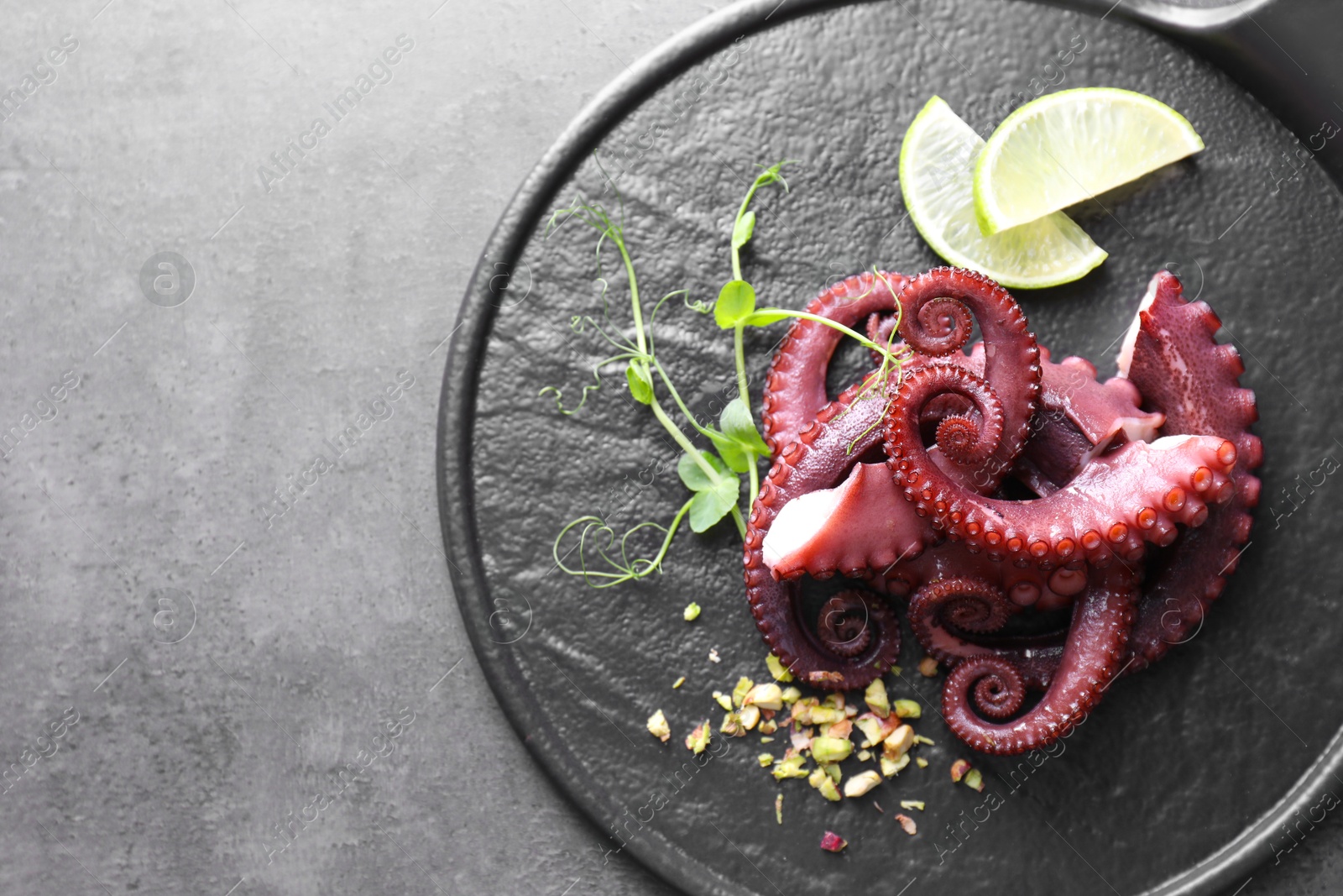 Photo of Tasty boiled octopus tentacles, microgreens, nuts and lime on grey table, top view. Space for text