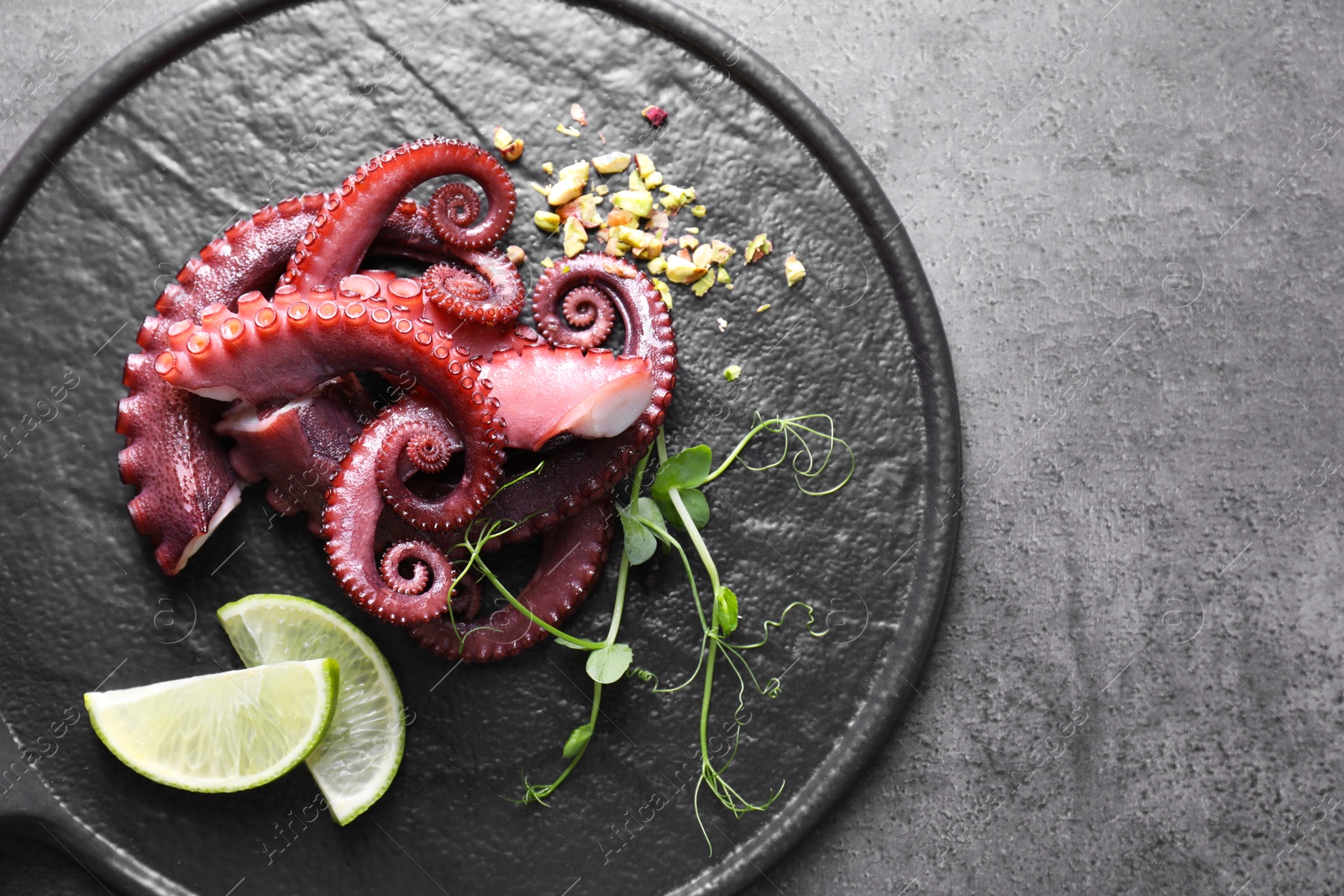 Photo of Tasty boiled octopus tentacles, microgreens, nuts and lime on grey table, top view. Space for text