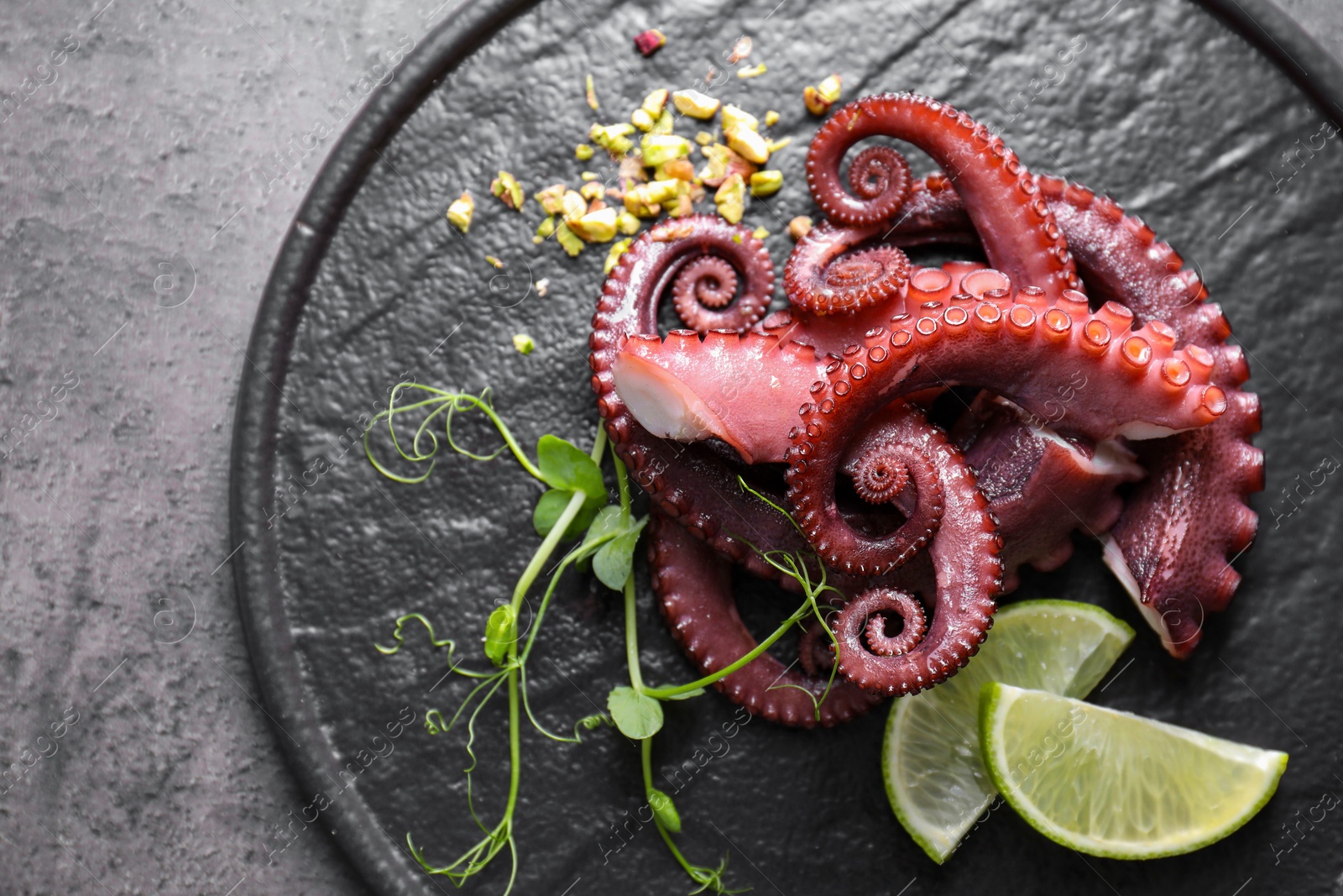 Photo of Tasty boiled octopus tentacles, microgreens, nuts and lime on grey table, top view. Space for text