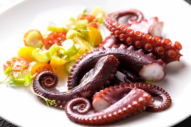 Photo of Tasty boiled octopus tentacles and salad on plate, closeup