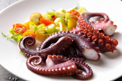 Photo of Plate with tasty boiled octopus tentacles and salad on grey table, closeup