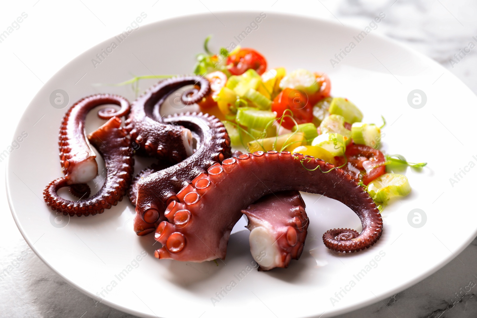 Photo of Plate with tasty boiled octopus tentacles and salad on white table, closeup