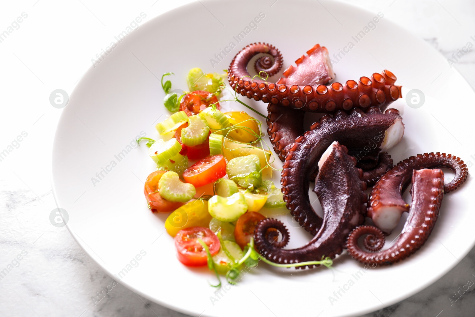 Photo of Plate with tasty boiled octopus tentacles and salad on white marble table, closeup