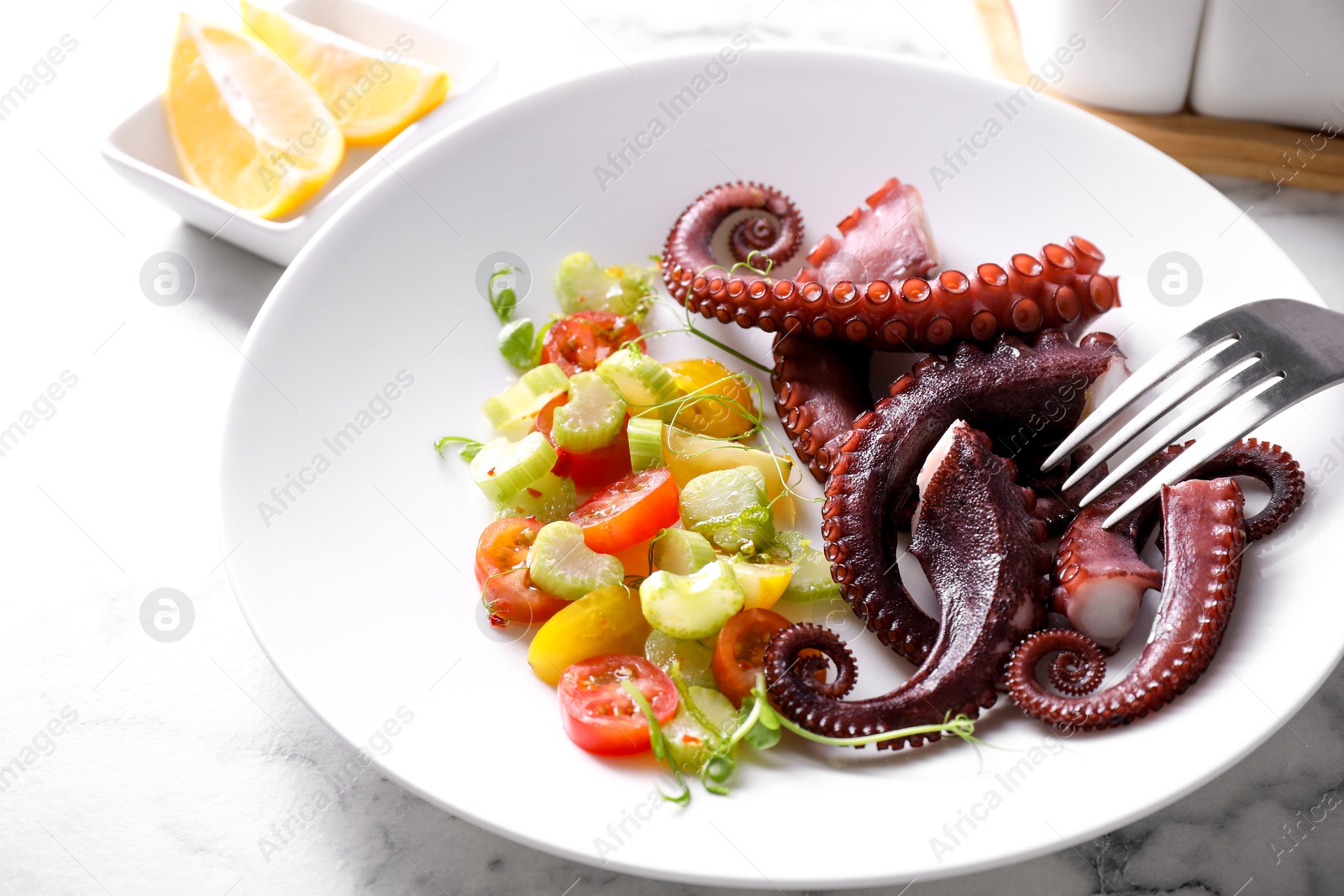 Photo of Plate with tasty boiled octopus tentacles, salad and fork on white marble table, closeup