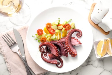 Photo of Tasty boiled octopus tentacles and salad served on white marble table, flat lay