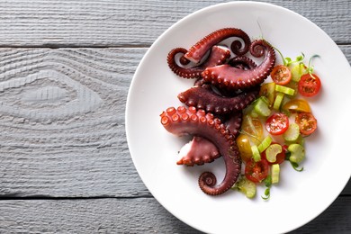 Photo of Plate with tasty boiled octopus tentacles and salad on grey wooden table, top view. Space for text