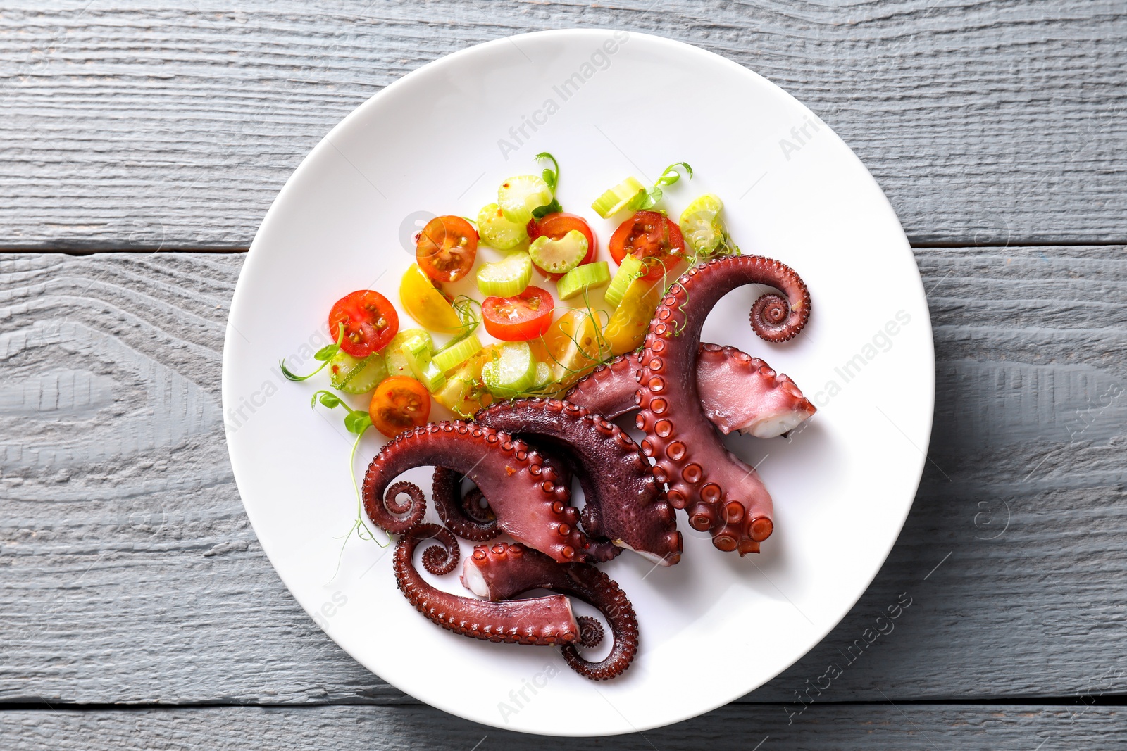 Photo of Plate with tasty boiled octopus tentacles and salad on grey wooden table, top view