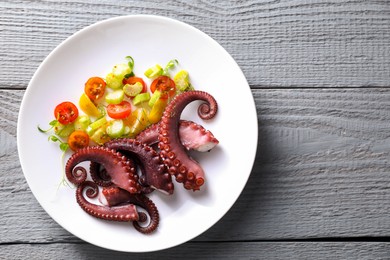 Photo of Plate with tasty boiled octopus tentacles and salad on grey wooden table, top view. Space for text