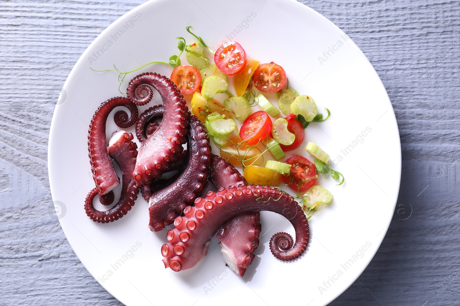 Photo of Plate with tasty boiled octopus tentacles and salad on grey wooden table, top view