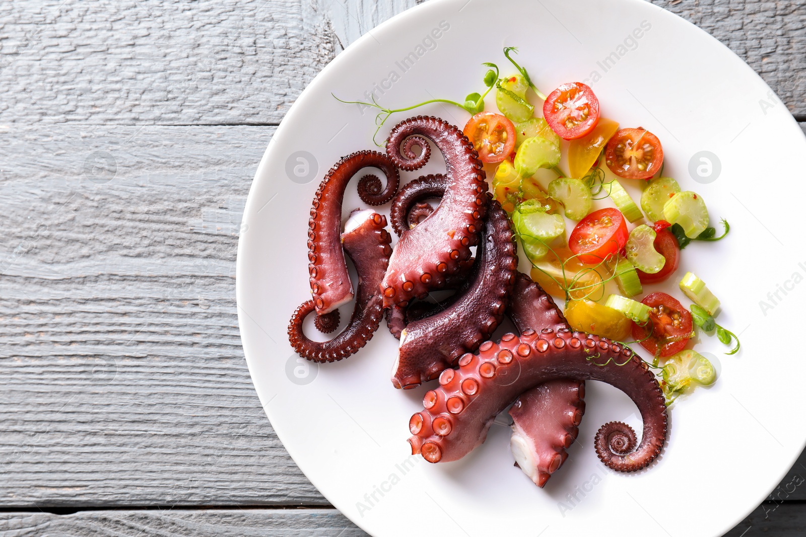 Photo of Plate with tasty boiled octopus tentacles and salad on grey wooden table, top view. Space for text