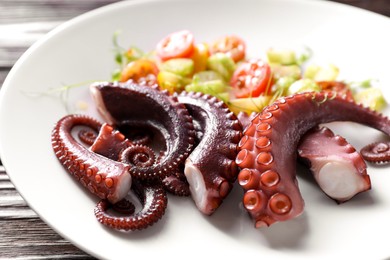 Photo of Plate with tasty boiled octopus tentacles and salad on wooden table, closeup