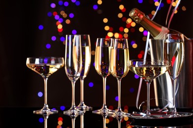 Champagne in glasses and ice bucket with bottle on mirror surface against dark background with blurred lights