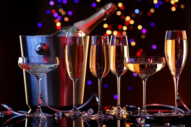 Photo of Champagne in glasses and ice bucket with bottle on mirror surface against dark background with blurred lights