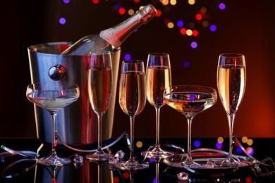 Champagne in glasses and ice bucket with bottle on mirror surface against dark background with blurred lights