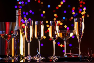 Photo of Champagne in glasses, bottle and ice bucket on mirror surface against dark background with blurred lights