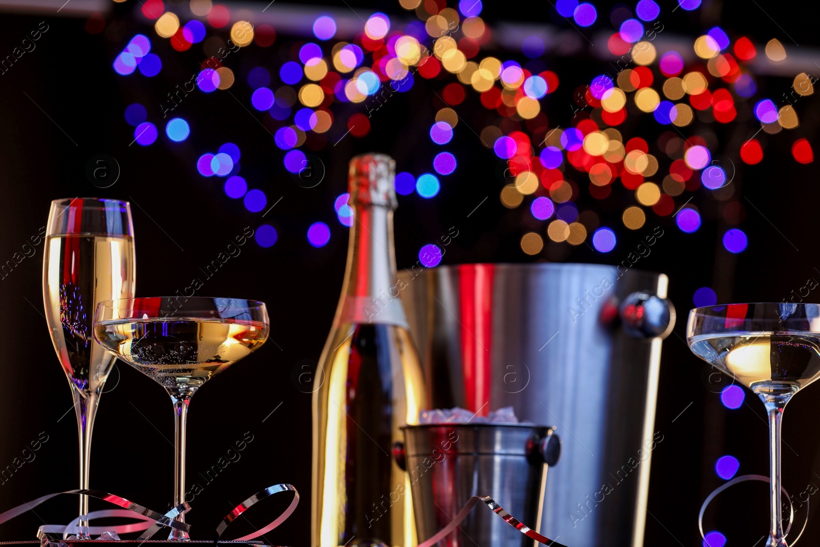 Photo of Champagne in glasses, bottle and ice buckets against black background with blurred lights