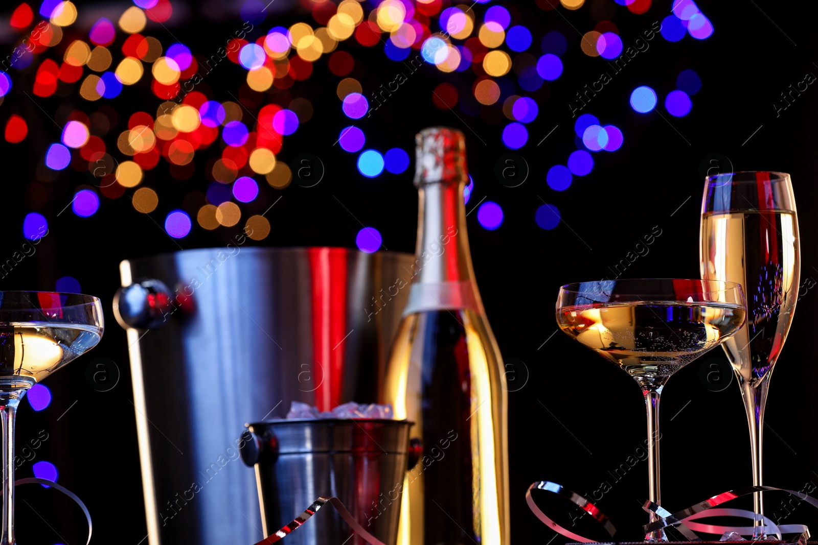 Photo of Champagne in glasses, bottle and ice buckets against black background with blurred lights