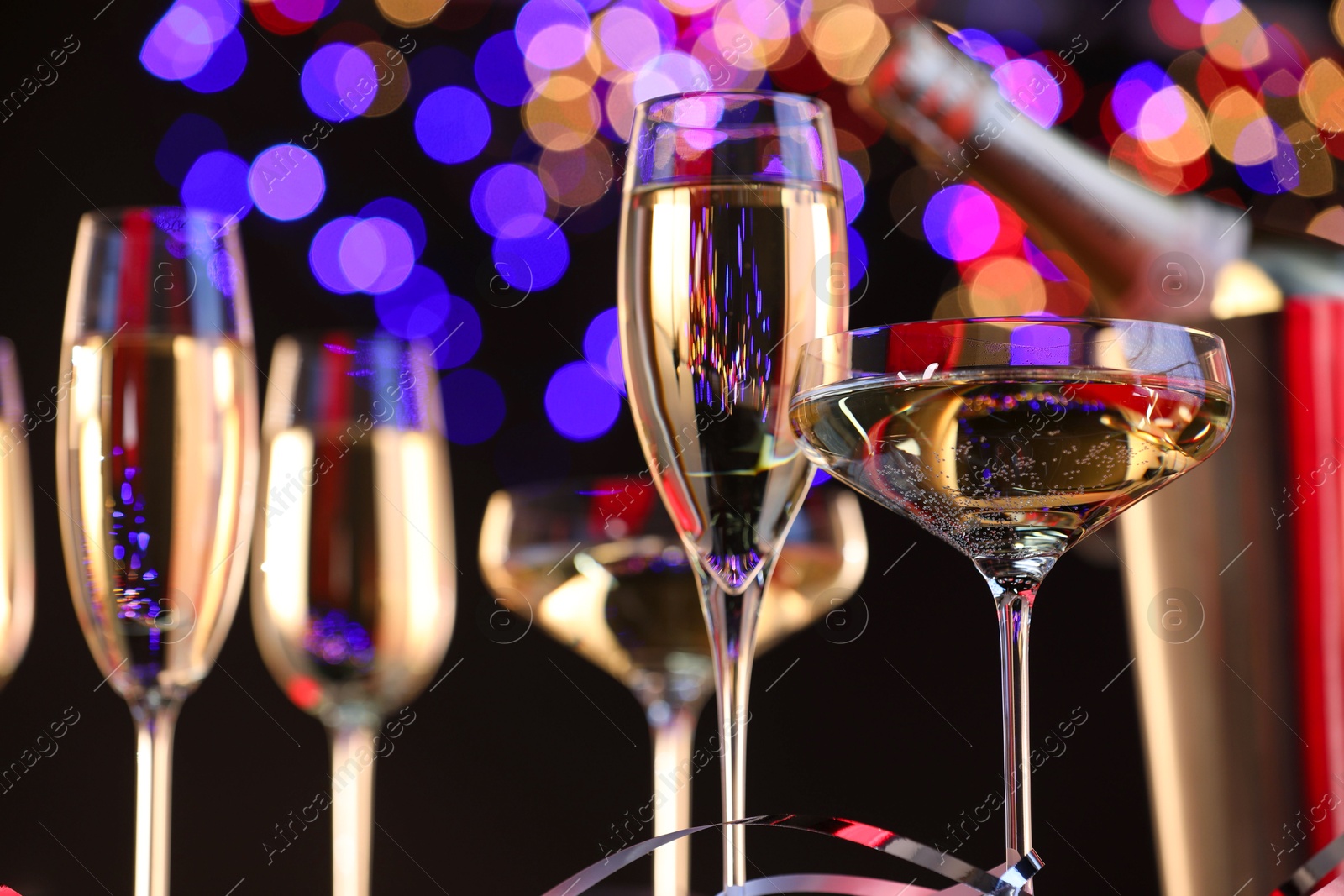 Photo of Champagne in glasses and party streamers against black background with blurred lights, low angle view