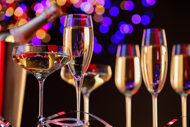 Photo of Champagne in glasses and party streamers against black background with blurred lights