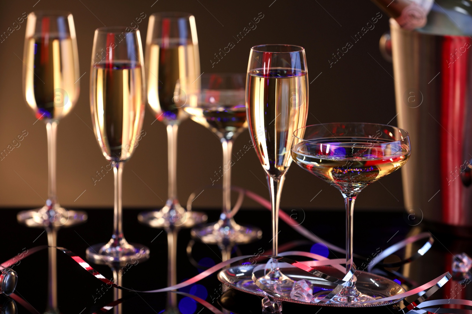 Photo of Champagne in glasses and party streamers on black mirror surface