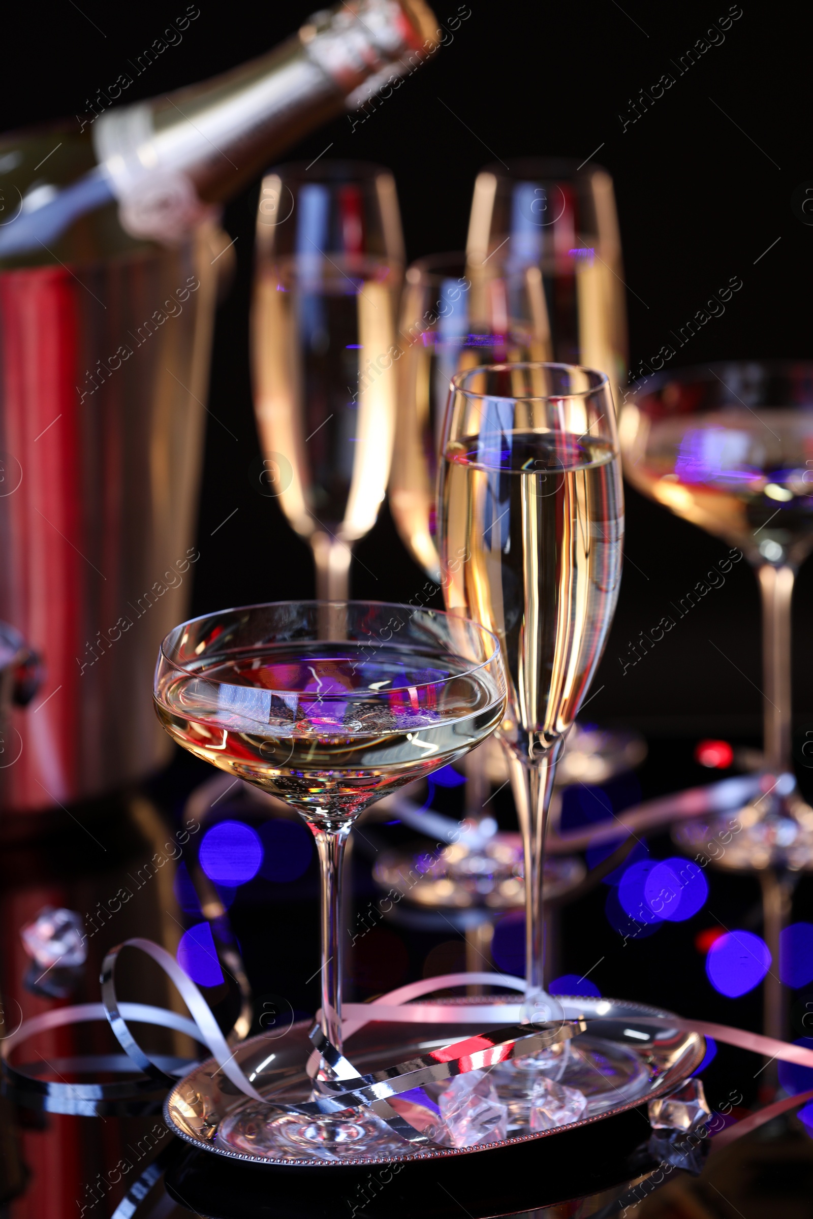 Photo of Champagne in glasses and party streamers on black mirror surface