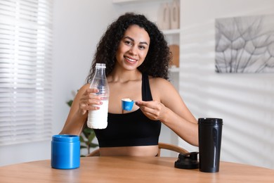 Photo of Beautiful woman making protein shake at wooden table indoors