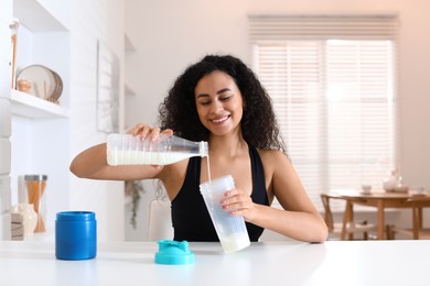 Photo of Beautiful woman making protein shake at white table indoors