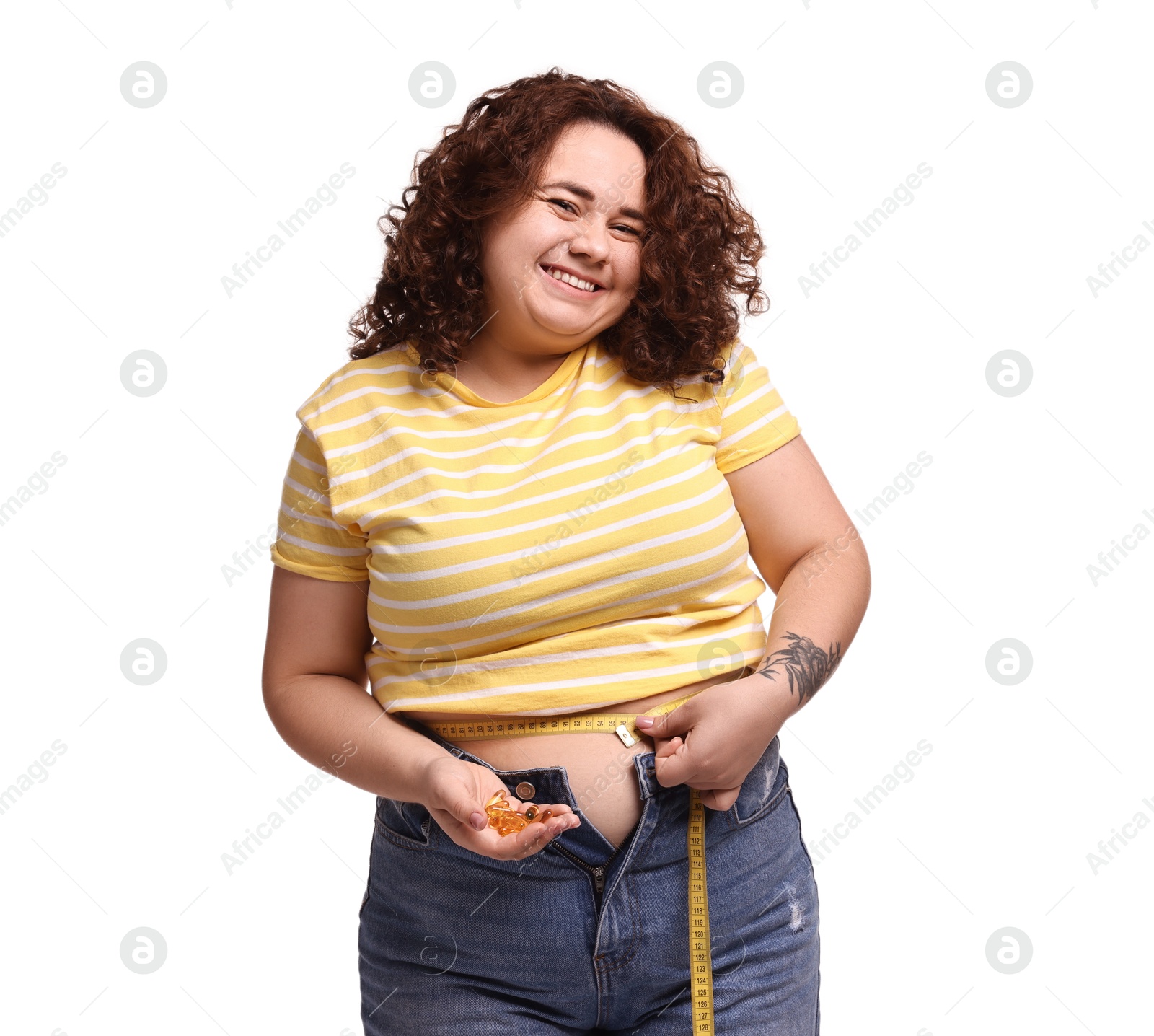 Photo of Happy plus size woman measuring waist with tape and holding pile of weight loss supplements on white background