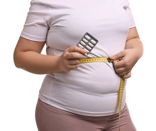 Photo of Plus size woman measuring waist with tape and holding blister of weight loss supplements on white background, closeup