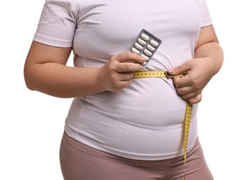 Photo of Plus size woman measuring waist with tape and holding blister of weight loss supplements on white background, closeup