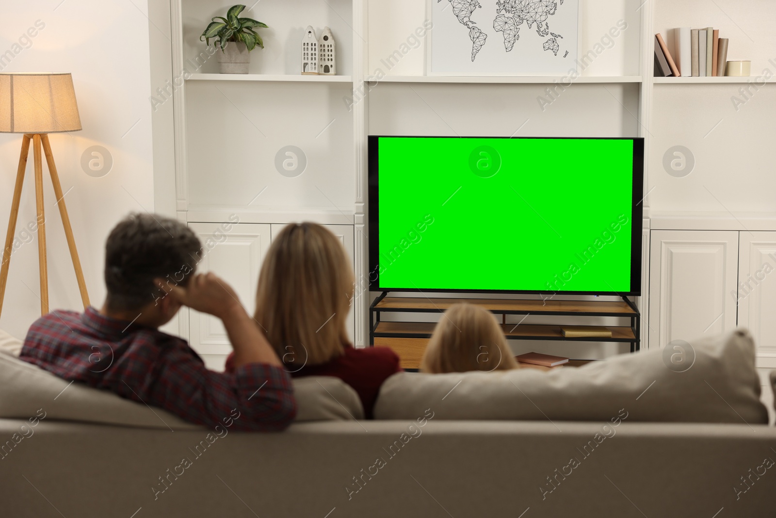 Photo of Family watching TV on sofa at home, back view