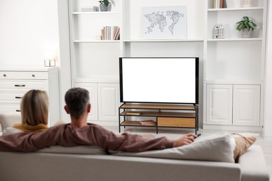 Photo of Couple watching TV on sofa at home, back view