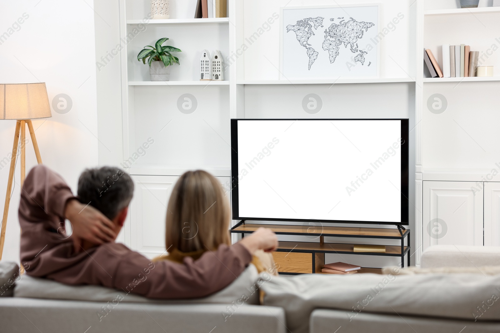 Photo of Couple watching TV on sofa at home, back view