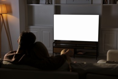 Photo of Couple watching TV on sofa at home in evening, back view