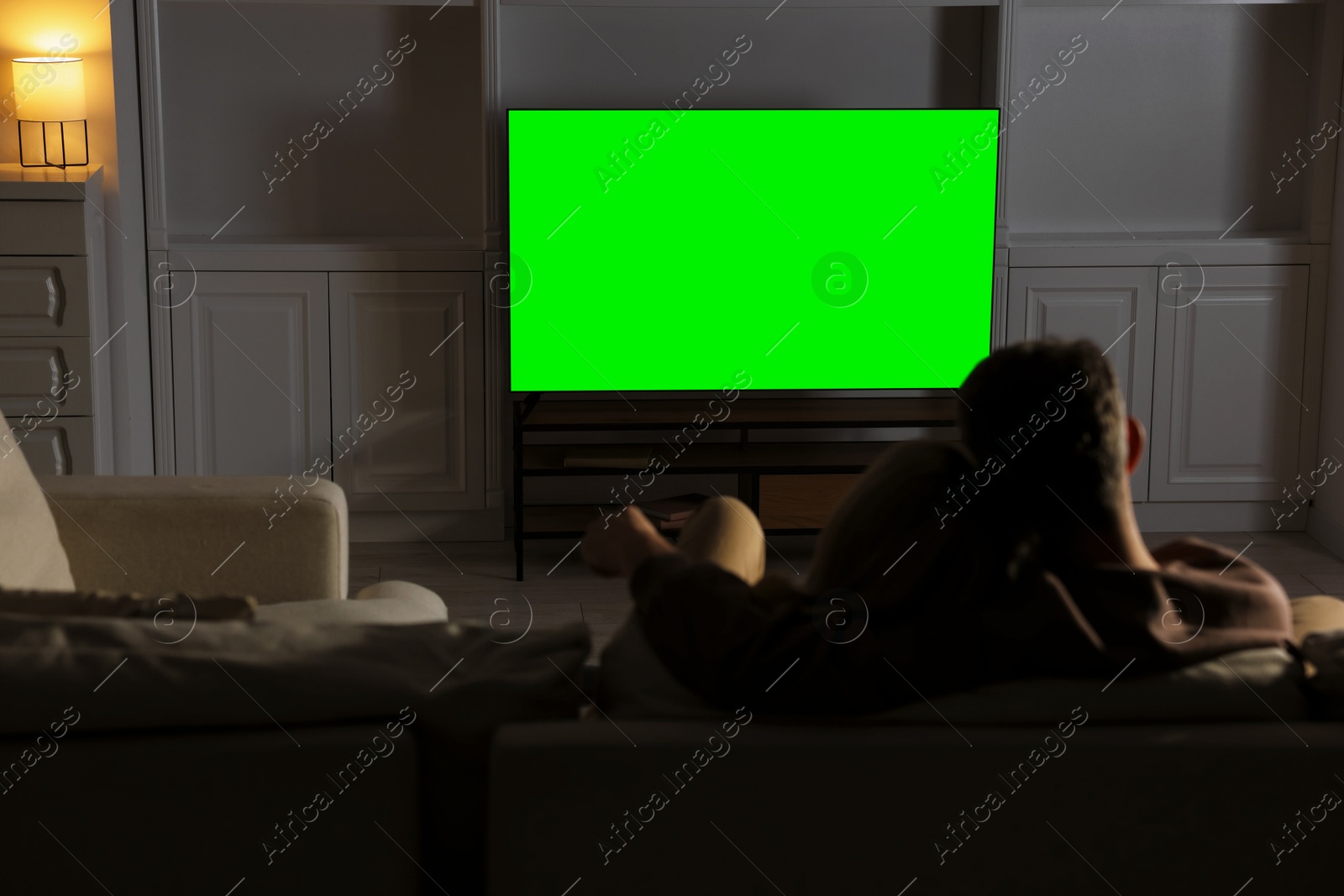 Photo of Couple watching TV on sofa at home in evening, back view