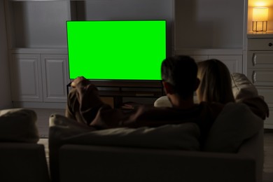 Photo of Couple watching TV on sofa at home in evening, back view